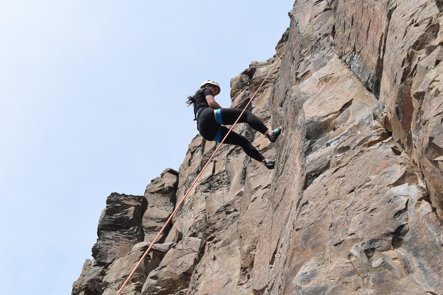 Climber leans slightly back and keeps their feet out to walk down the rock while being lowered by the belayer